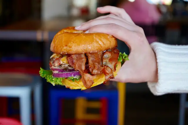 A bacon cheeseburger stacked with red onion and lettuce