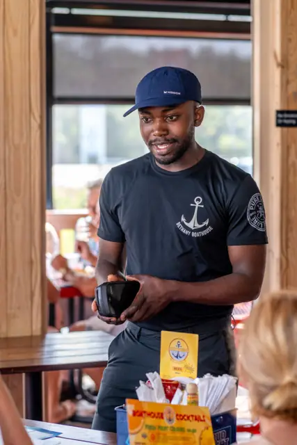 Boathouse server in an anchor tee taking a table's order